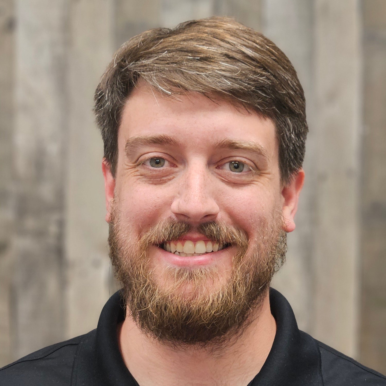 Man wearing a black shirt with a logo, standing against a blurred background