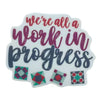 We're All a Work in Progress sticker with script lettering and four quilt blocks